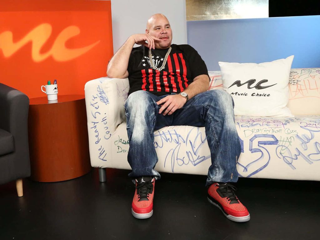 Fat Joe studio portrait on Music Choice couch wearing red Air Jordans with orange blue backdrop Wallpaper