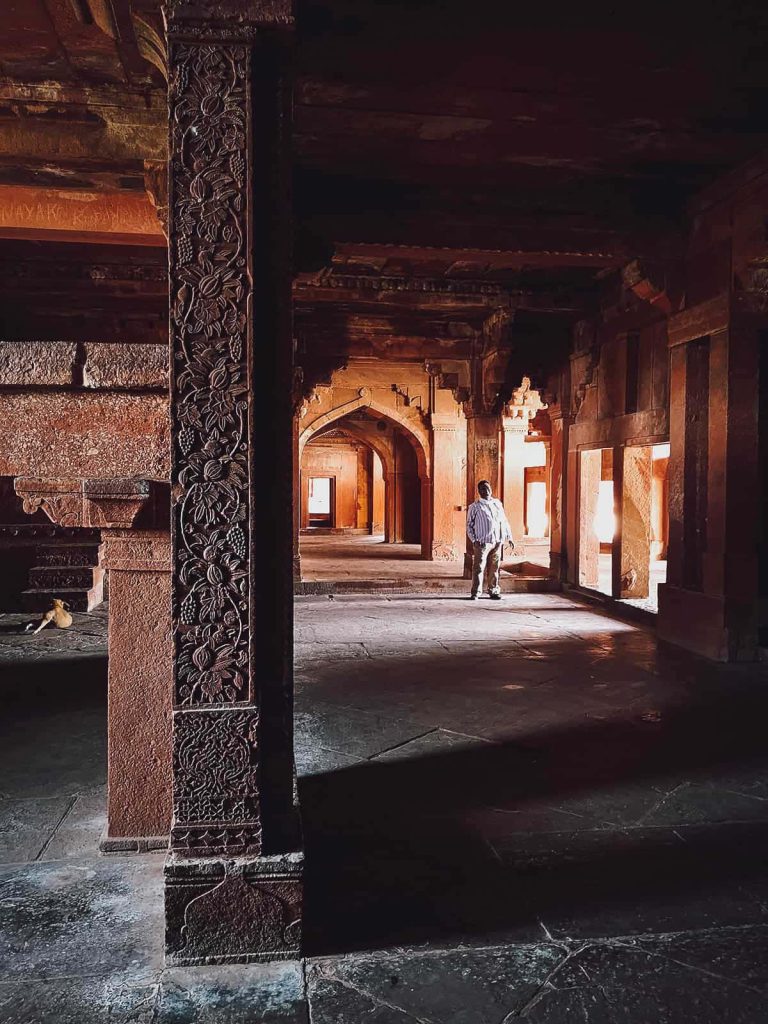 Man in sunlit red sandstone corridor of Fatehpur Sikri showcasing Mughal architecture detail Wallpaper