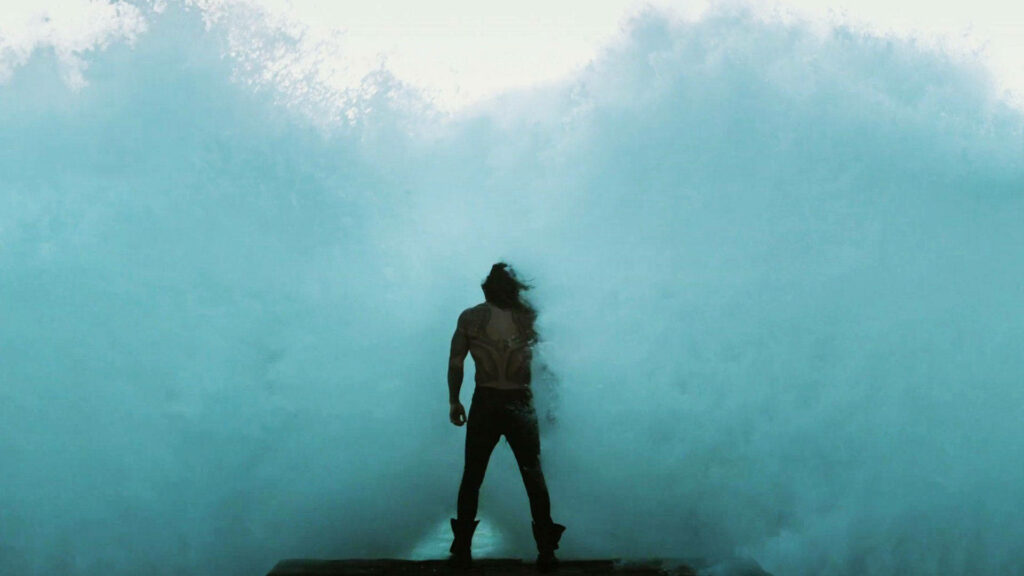 Arthur Curry Aquaman stands boldly on pier facing giant crashing wave stormy sky wallpaper