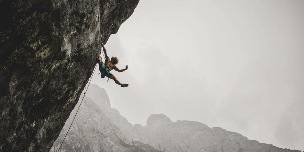 Daring climber on steep cliff with stormy skies and rugged mountains adventurous wallpaper