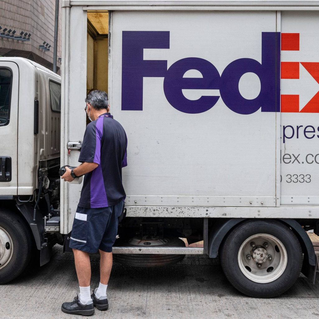 FedEx delivery driver in uniform with scanner by white truck showing package delivery process Wallpaper