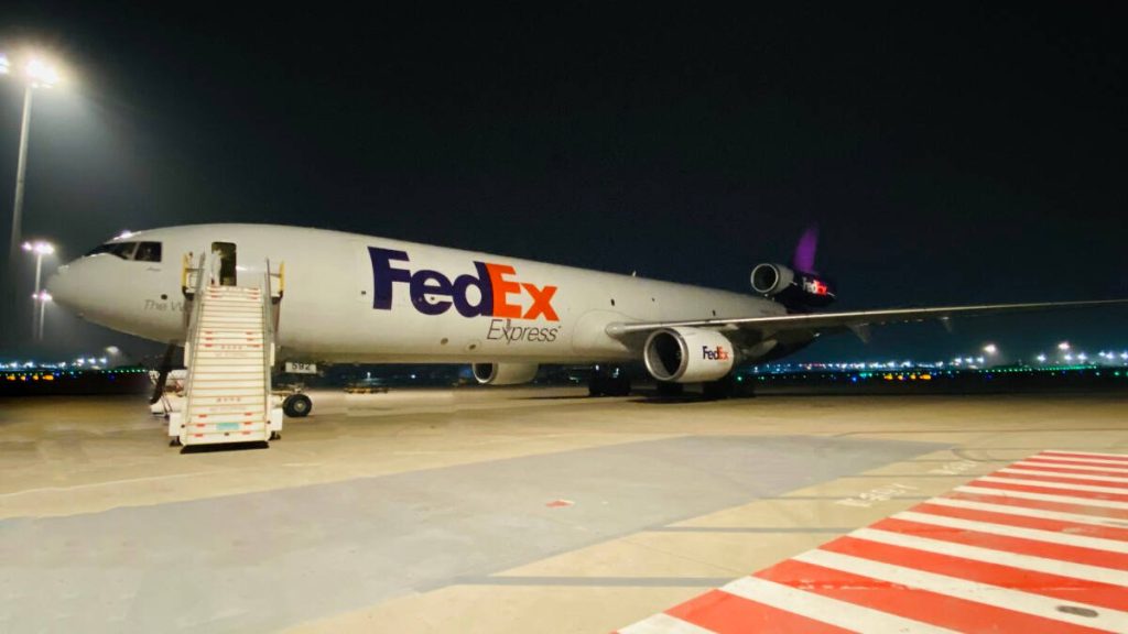 FedEx Express cargo plane on tarmac at night with bright floodlights and mobile staircase Wallpaper