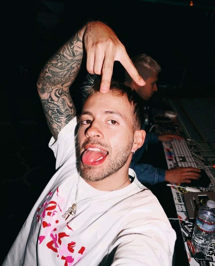 Colombian singer Feid flash-lit studio portrait with arm tattoos playful pose high-contrast wallpaper
