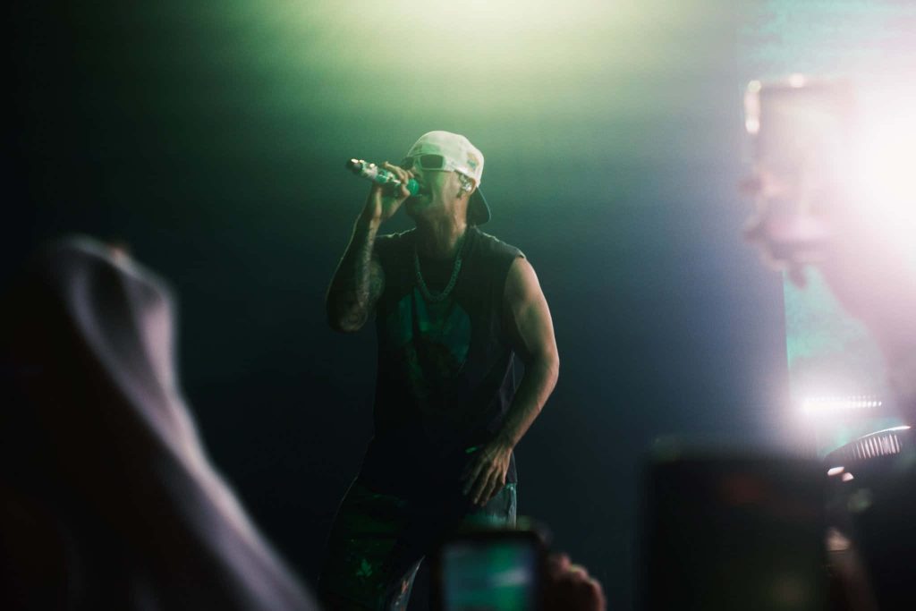 Colombian singer Feid performing live on stage with green lighting and signature white cap Wallpaper