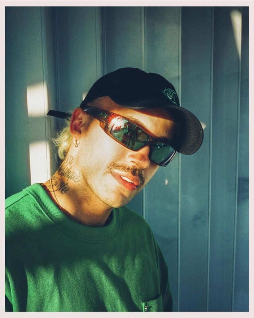 Feid Colombian singer confident pose green sweatshirt black cap sunglasses warm sunlight wallpaper