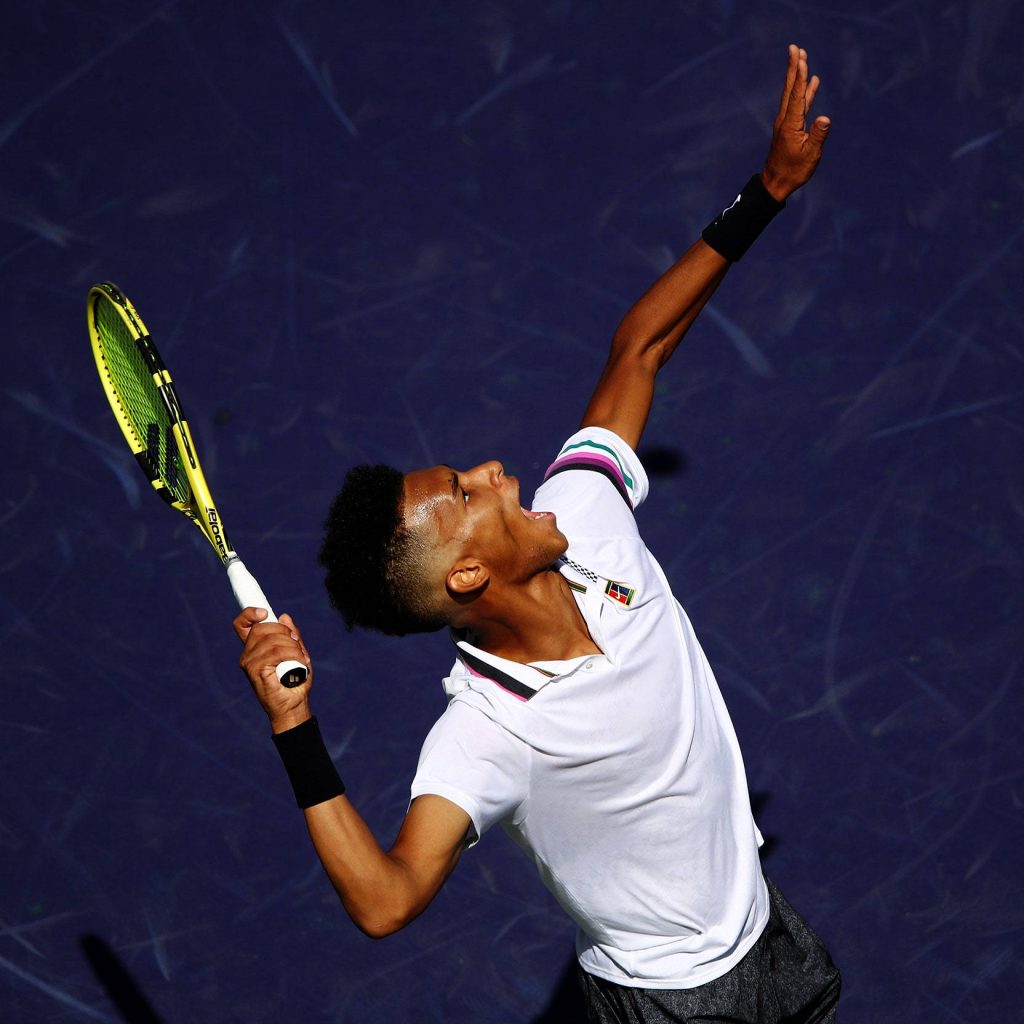 Felix Auger Aliassime serving on blue court in white polo with yellow Babolat racket action shot Wallpaper