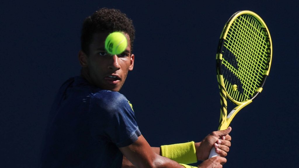Tennis star Felix Auger Aliassime mid-swing with neon yellow racket in dark gear wallpaper background