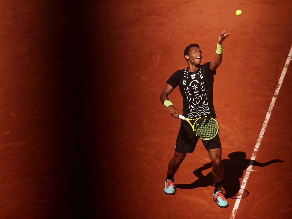 Felix Auger-Aliassime serving on red clay court dynamic action shot bright sunlight wallpaper