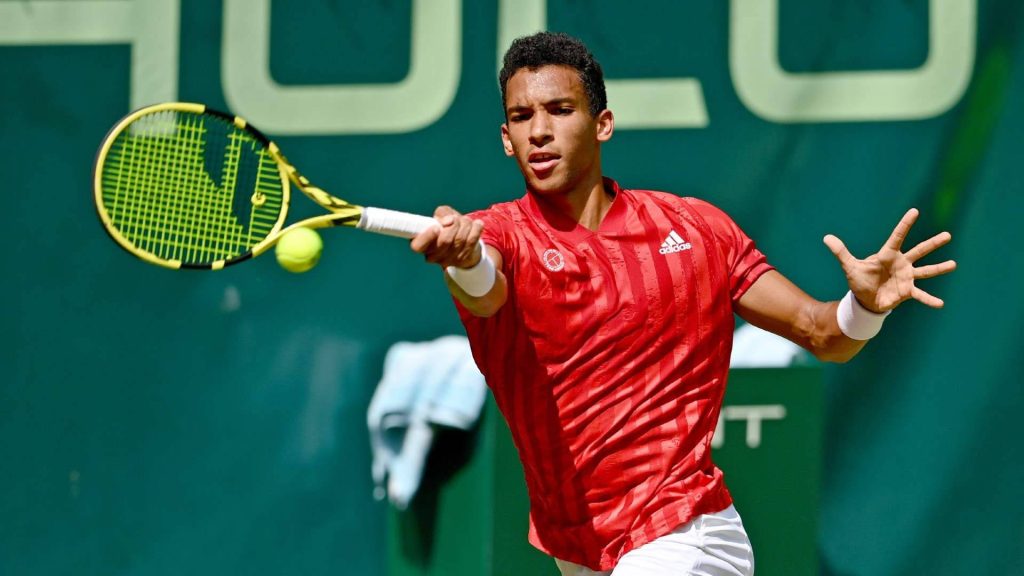 Félix Auger Aliassime powerful forehand in red Adidas on green tennis court with Hulu branding wallpaper
