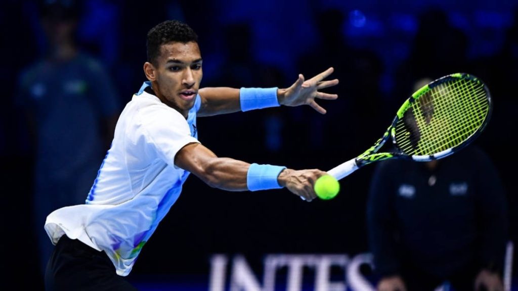 Félix Auger-Aliassime hits powerful forehand in white blue kit under arena lighting action shot Wallpaper