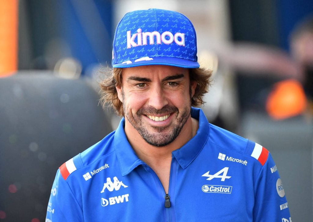 Formula 1 legend Fernando Alonso in Alpine blue polo and Kimoa cap smiling in paddock Wallpaper
