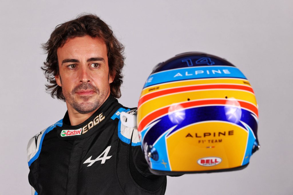 Fernando Alonso in black Alpine race suit holding blue yellow helmet studio portrait gray background Wallpaper