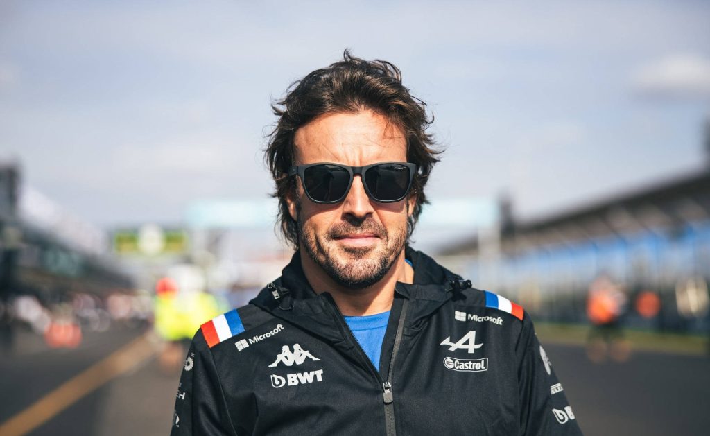 Fernando Alonso in black Alpine F1 jacket and sunglasses at racetrack vibrant portrait wallpaper
