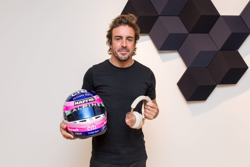 Fernando Alonso with Alpine racing helmet and Bang Olufsen headphones in studio portrait Wallpaper