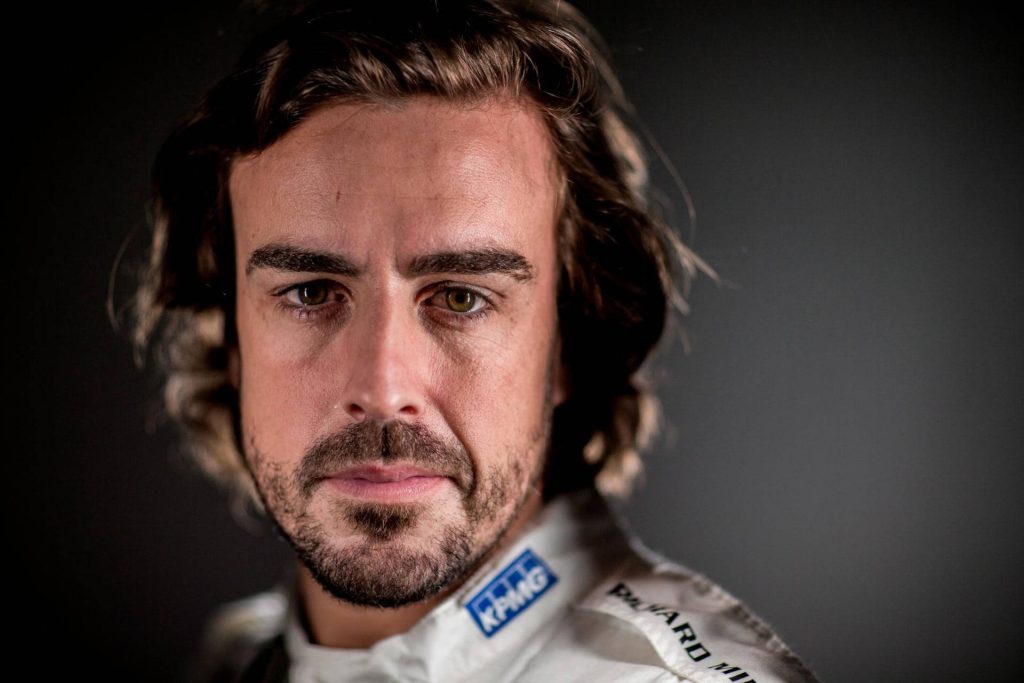 Close-up portrait of F1 champion Fernando Alonso in white KPMG racing suit on dark backdrop Wallpaper