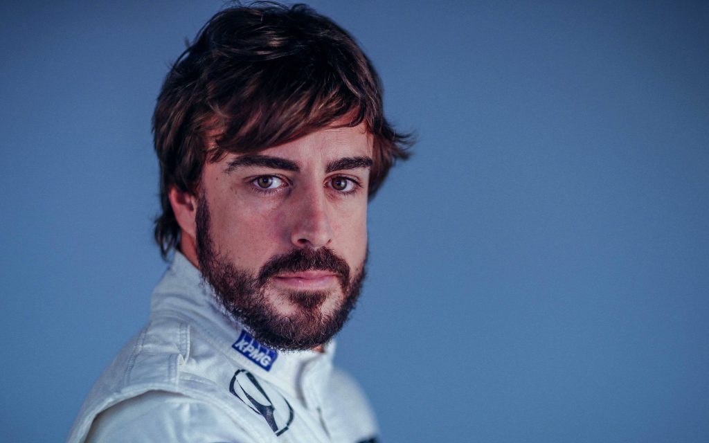 Fernando Alonso F1 close-up portrait in white racing suit with focused intense gaze blue background Wallpaper