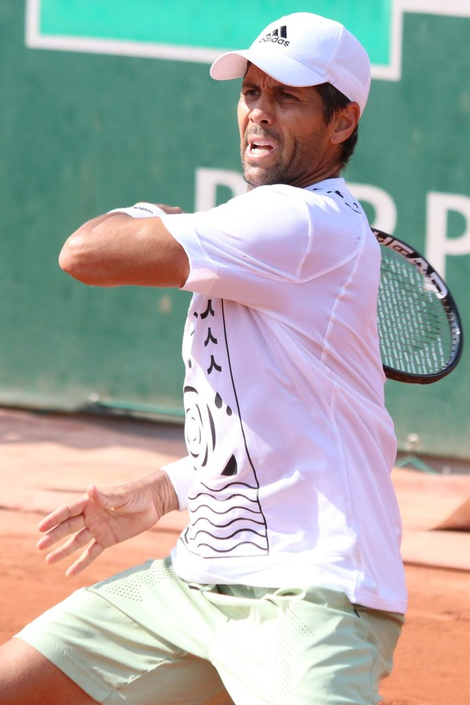 Fernando Verdasco tennis forehand on red clay court in white Adidas cap and graphic tee Wallpaper