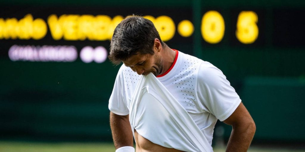 Fernando Verdasco tennis player pulling white shirt on court with green scoreboard background wallpaper