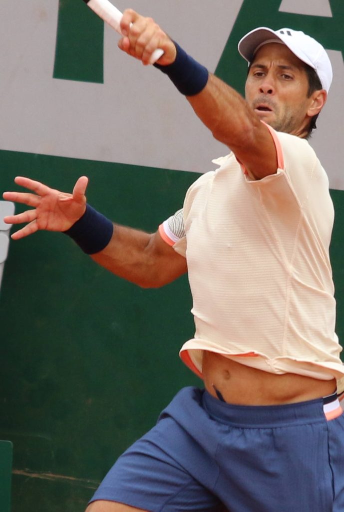 Fernando Verdasco mid-forehand swing in peach shirt and white cap on green tennis court background Wallpaper