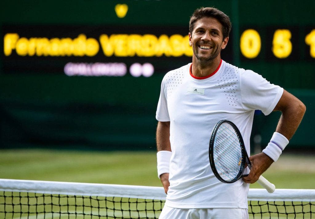 Fernando Verdasco smiling by net in white gear tennis wallpaper with green tournament scoreboard