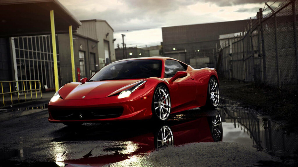 Ferrari 458 Rosso Corsa in industrial setting with sleek red body reflected on wet pavement Wallpaper