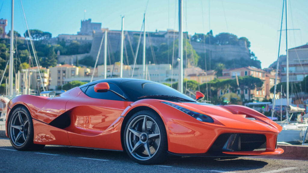 Red Ferrari LaFerrari Spider parked by marina with yachts and historic fort background wallpaper
