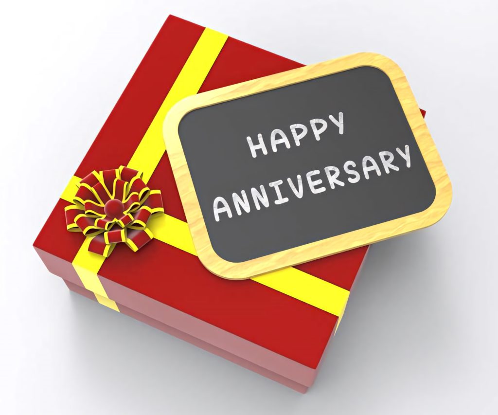Festive 3D red gift box with yellow ribbon and chalkboard saying Happy Anniversary on white background Wallpaper