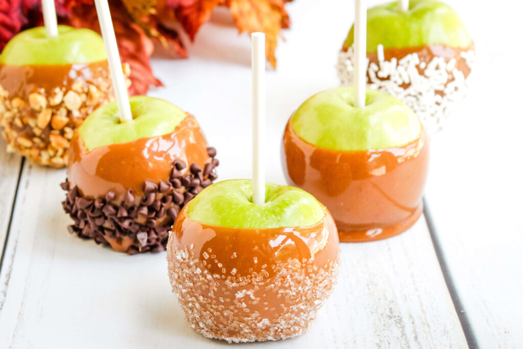Caramel apples with nuts and sprinkles on rustic white table in warm autumn lighting wallpaper
