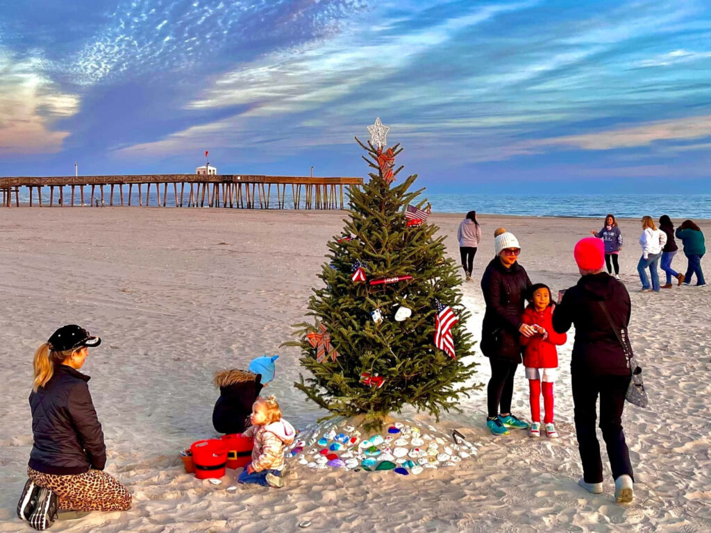 Festive Beach Scene: Christmas Tree & People Celebrating by Ocean Wallpaper