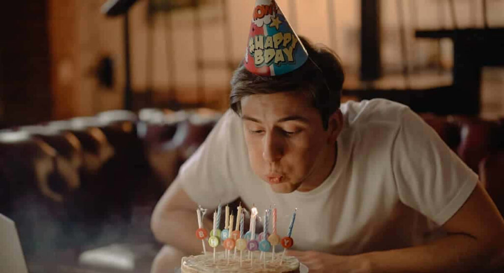 Cozy Birthday Celebration: Man Blowing Out Colorful Cake Candles Wallpaper