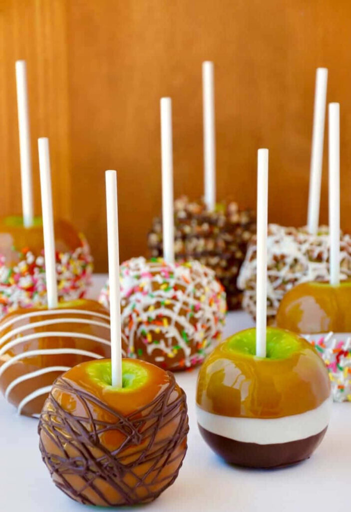 Caramel apples with sprinkles chocolate drizzle and nuts on rustic autumn table wallpaper background