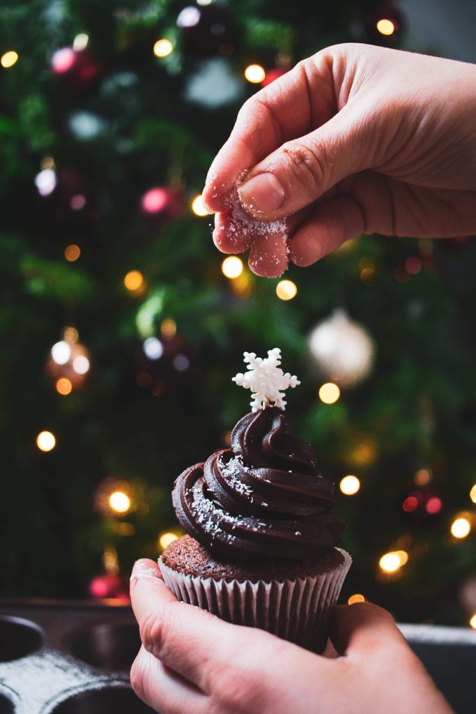 Festive chocolate Christmas cupcake with snowflake and holiday tree bokeh wallpaper background