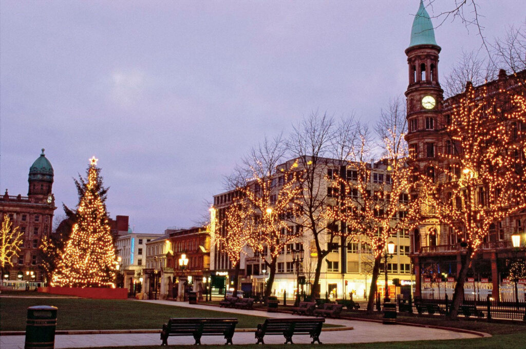 Enchanting Holiday Cityscape with Twinkling Lights and Christmas Tree Wallpaper