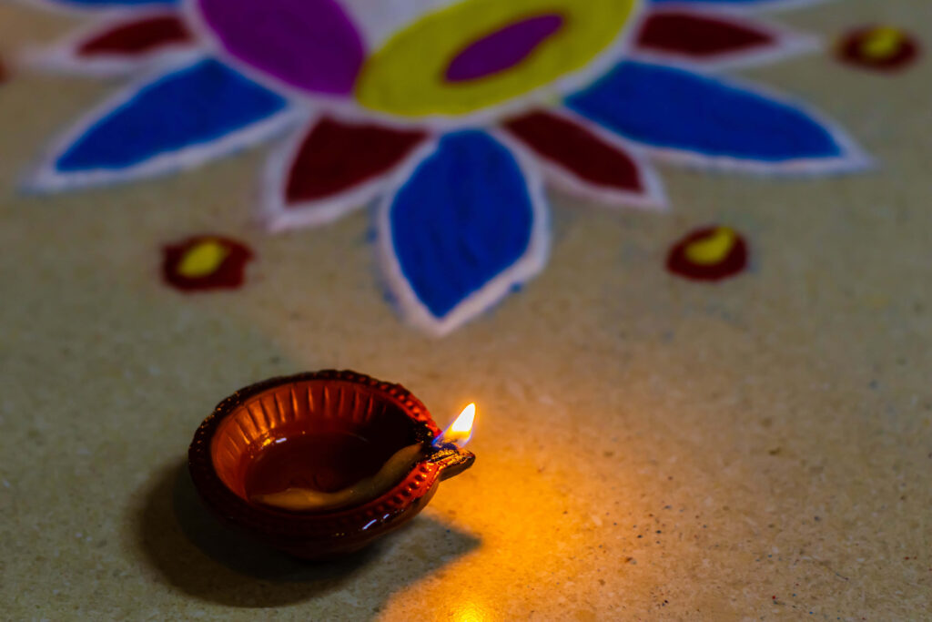 Traditional clay candle glowing beside vibrant blue red yellow Rangoli for Diwali celebration Wallpaper