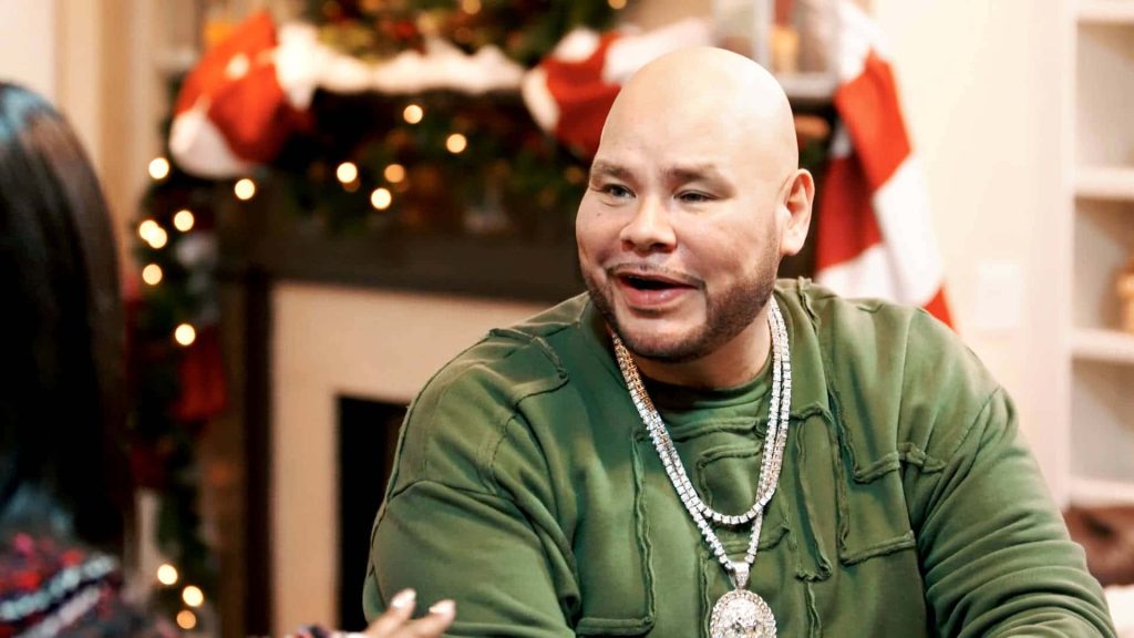 Festive Fat Joe in green shirt with diamond chains against Christmas lights and stockings background Wallpaper