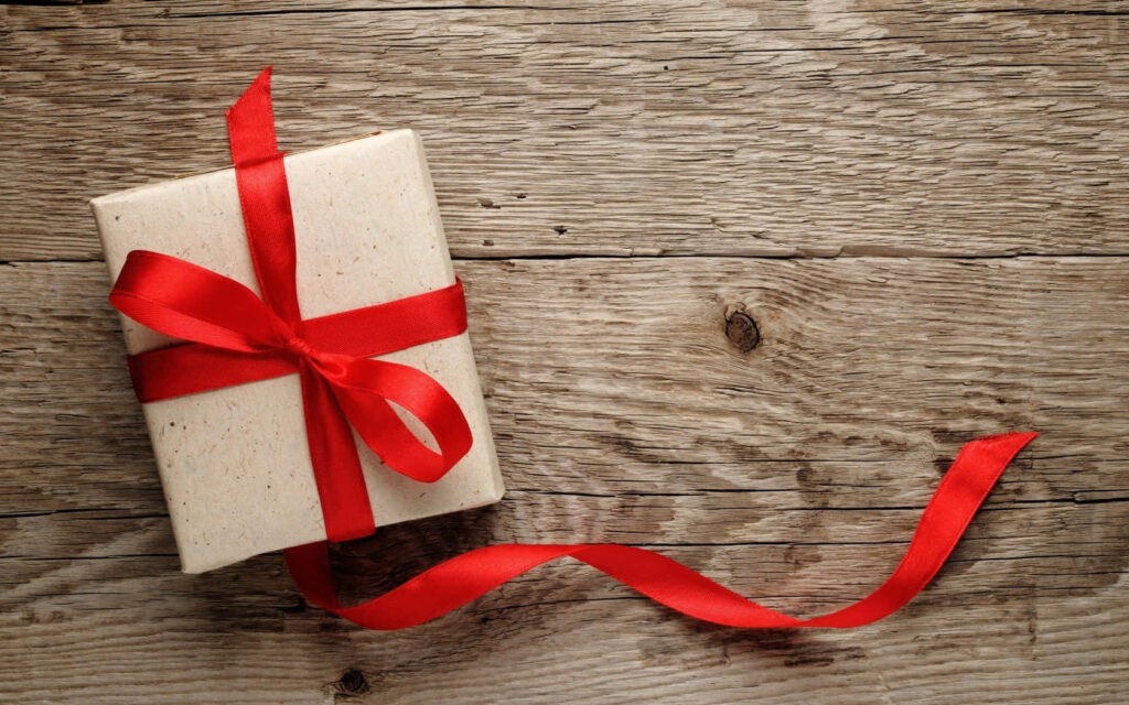Neatly wrapped gift box with bright red ribbon on rustic wooden surface festive holiday present Wallpaper