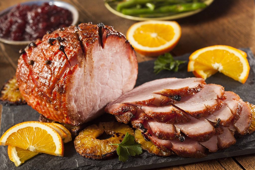 Festive clove-studded glazed ham with grilled pineapple orange slices and parsley on slate board Wallpaper