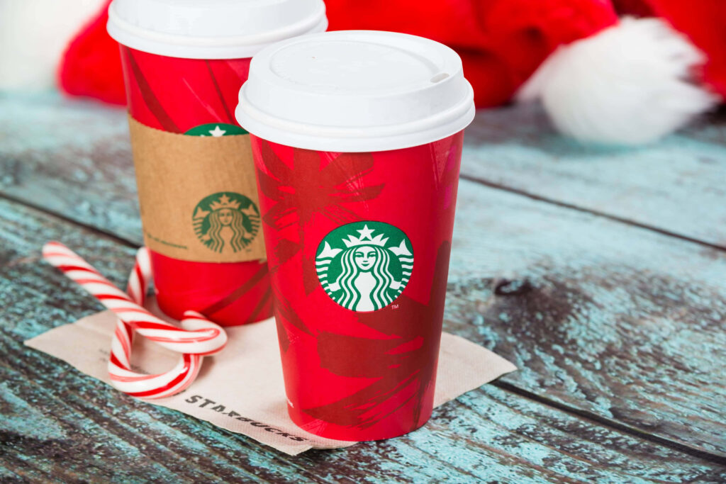 Starbucks red holiday cups with warm coffee and candy canes on rustic wooden table background Wallpaper