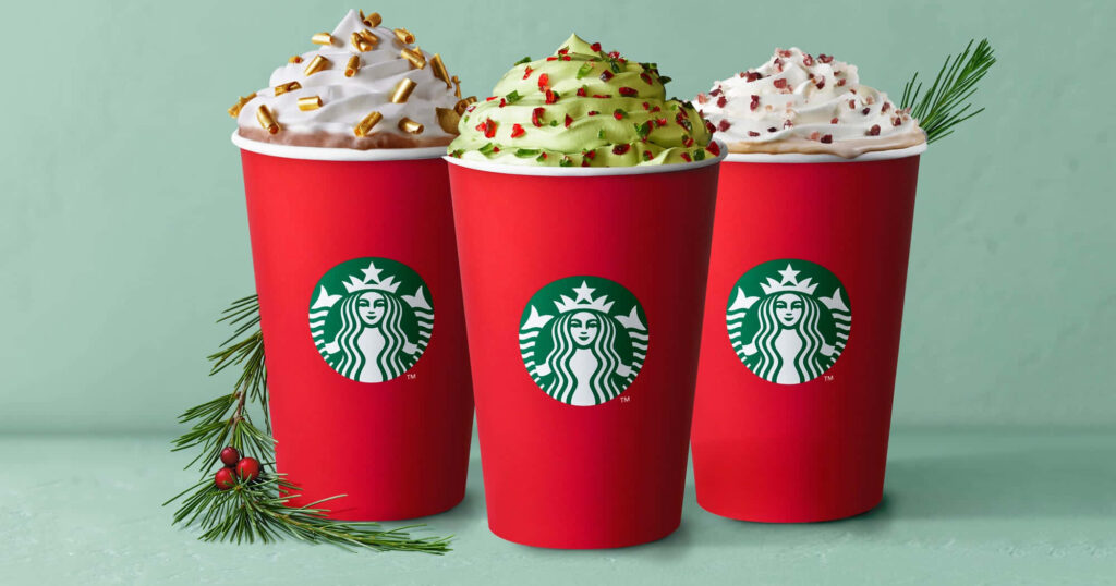 Festive Starbucks wallpaper with three red holiday cups topped with colorful whipped cream toppings