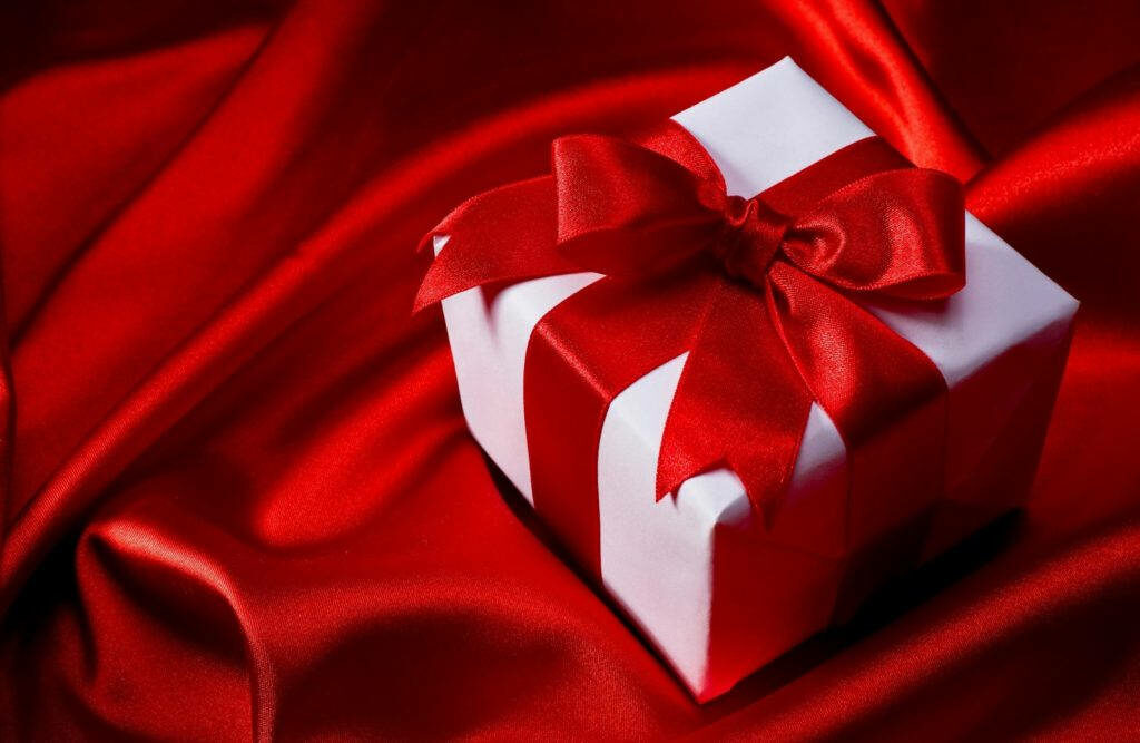 Elegant White Gift with Red Ribbon on Luxurious Satin Background Wallpaper