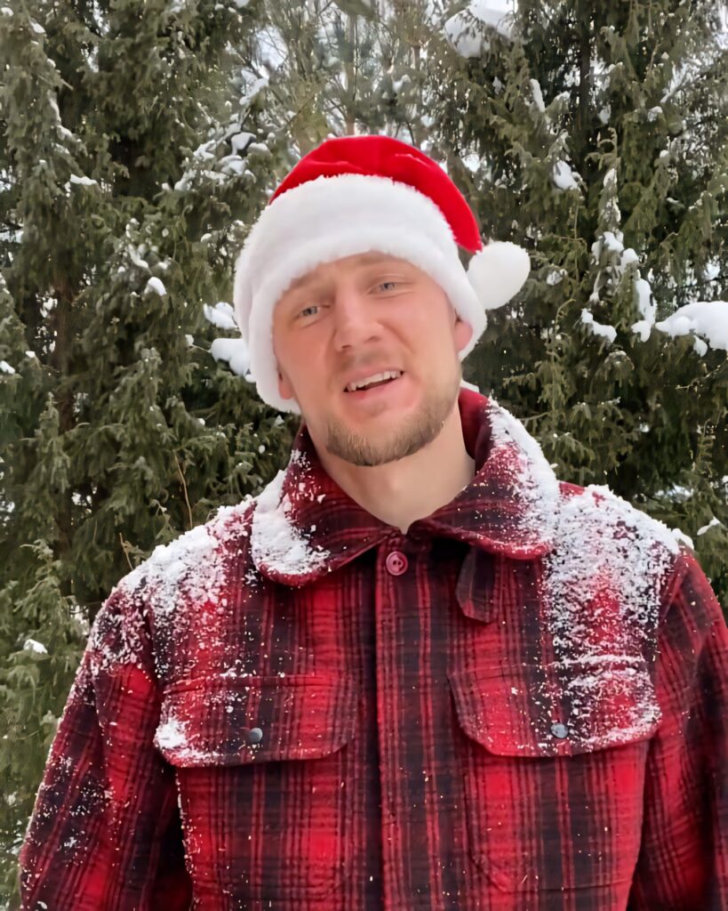 Festive Winter Scene: Person in Santa Hat & Plaid Jacket Amid Snowy Evergreens Wallpaper