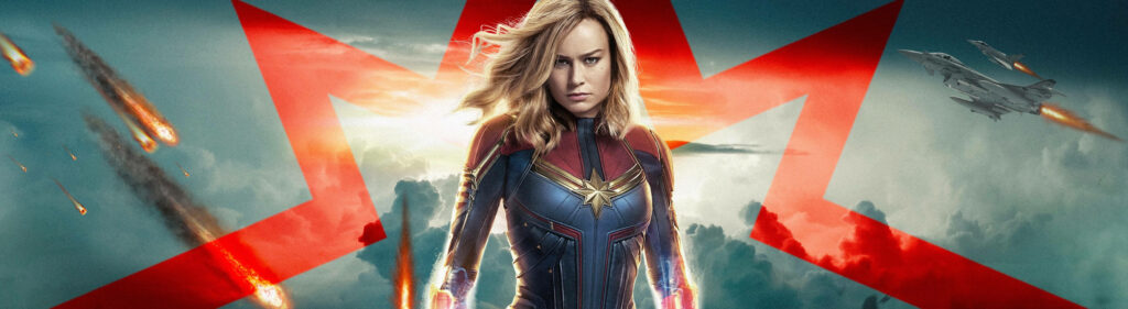 Explosive Power: Captain Marvel Strikes a Fierce Pose in Vibrant Red and Blue Costume - 5120 x 1440 Graphic Wallpaper
