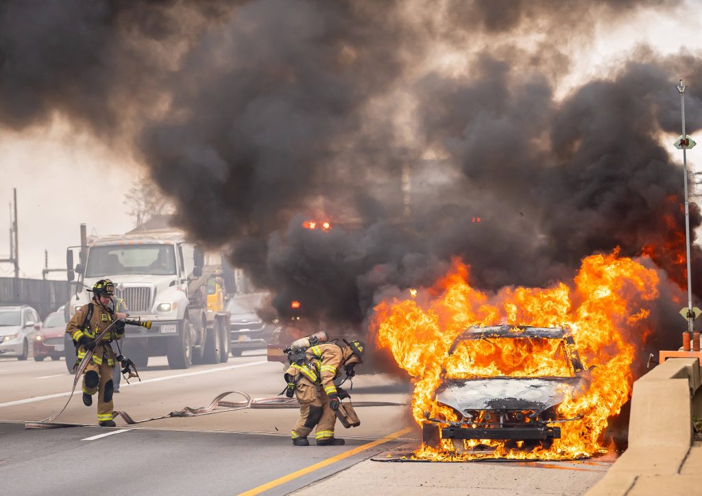 Firefighters battling blazing car fire on highway with thick black smoke urgent emergency scene Wallpaper