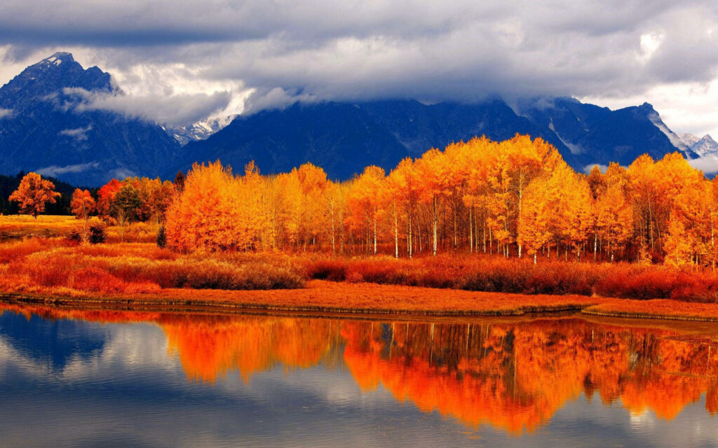 Autumn landscape with vibrant fall foliage reflected on calm lake under cloudy mountain sky wallpaper