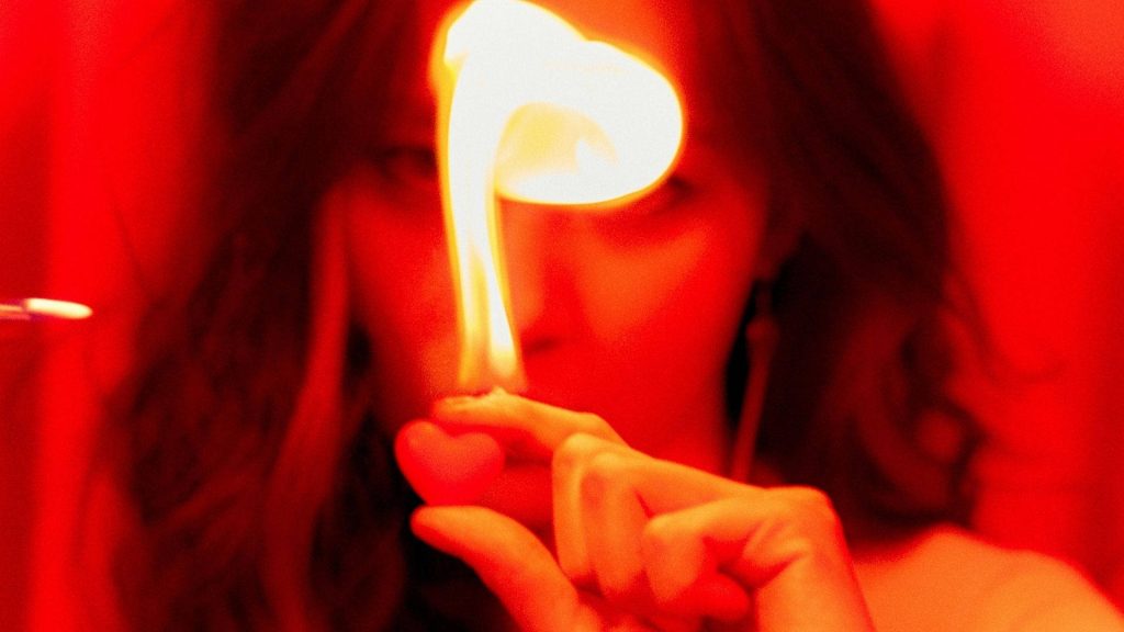 Close-up of hand holding heart-shaped object with fiery red flame moody wallpaper background