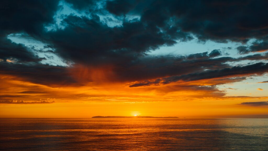 Tranquil sea at sunset with fiery orange sky and dark clouds creating dramatic contrast wallpaper