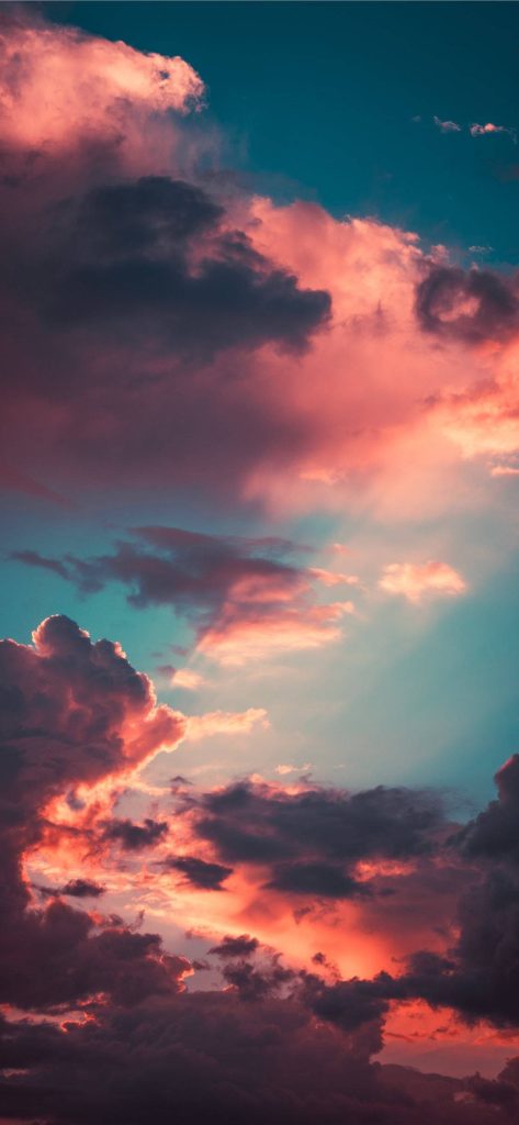 Fiery orange and pink clouds with light rays over a deep teal horizon morning sky wallpaper