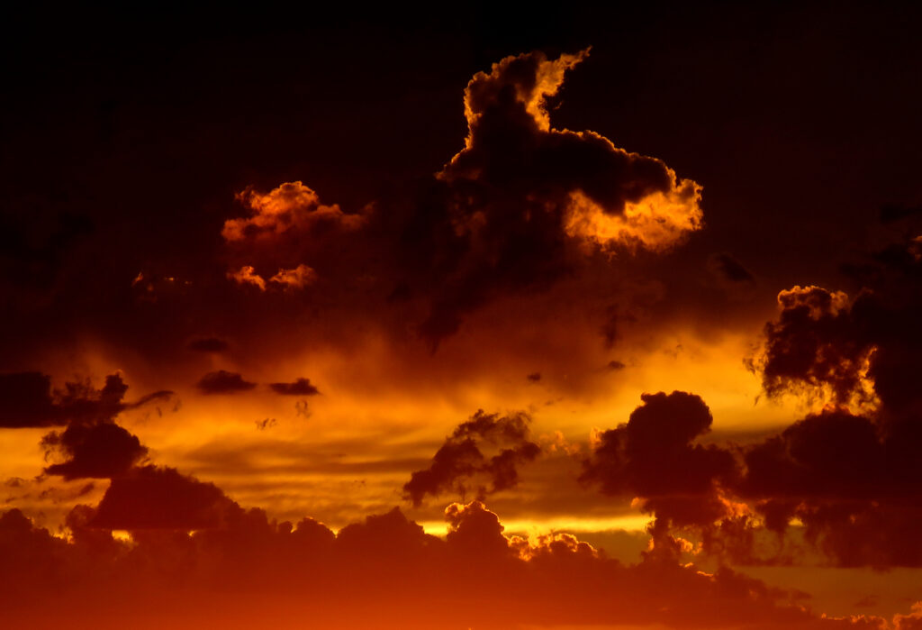 Dramatic dark clouds with fiery red and golden light against night sky moody wallpaper background