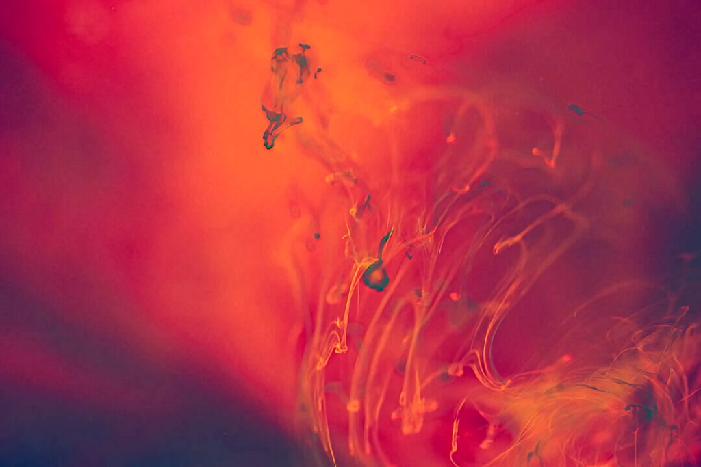 Abstract red and orange liquid swirls blend in water creating fiery fluid art wallpaper background