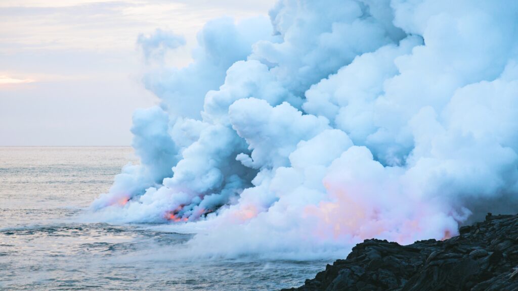 Thick white smoke over ocean with glowing fire and jagged dark rocks in dramatic nature scene Wallpaper